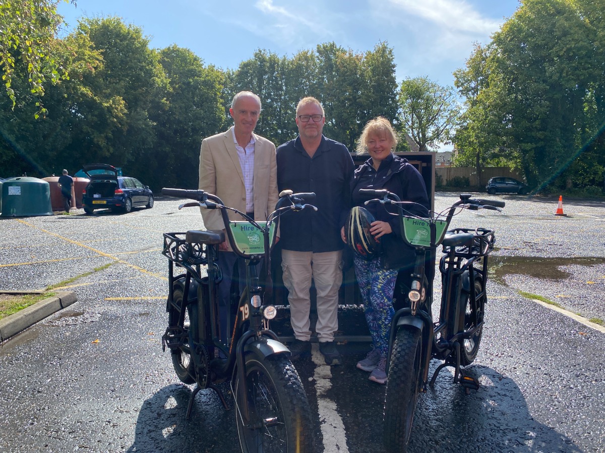 Cllr Paul Clover, ward member for Lavenham, Simon Cooper, EEZYBIKE founder, and Cllr Helen Davies, cabinet member for climate change, nature recovery and biodiversity, at EEZYBIKE's e-bike pod in Lavenham